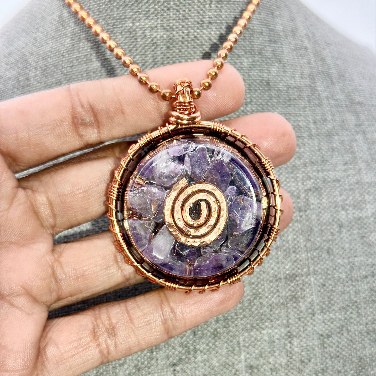 Amethyst spiral pendant necklace held in a hand against a gray background