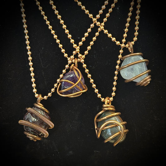 Four copper necklaces with stone pendants on a black background