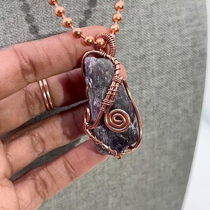 Hand holding and rotating copper wire wrapped purple amethyst crystal